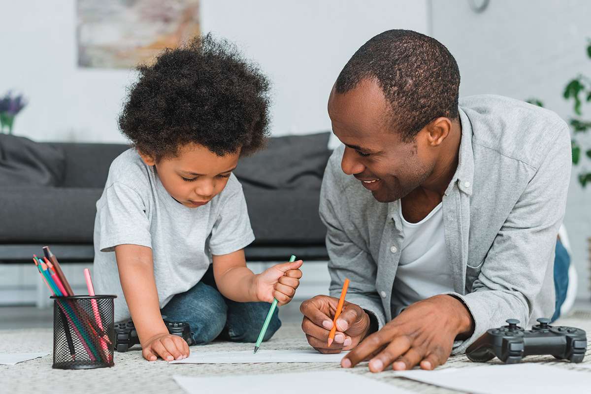 A father and son engage in drawing on the floor, illustrating the joy of family bonding and creativity in 2025.