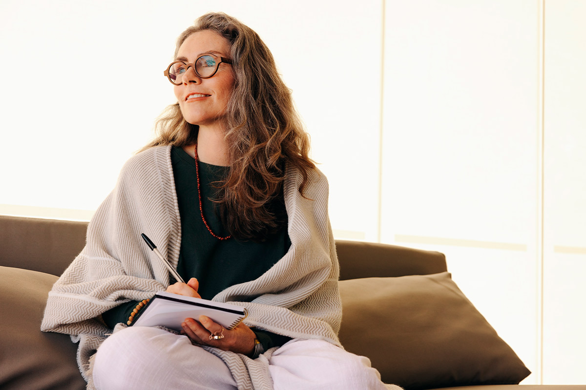 A woman sits cross-legged in a living room, meditating as part of her mindfulness and gratitude routine.
