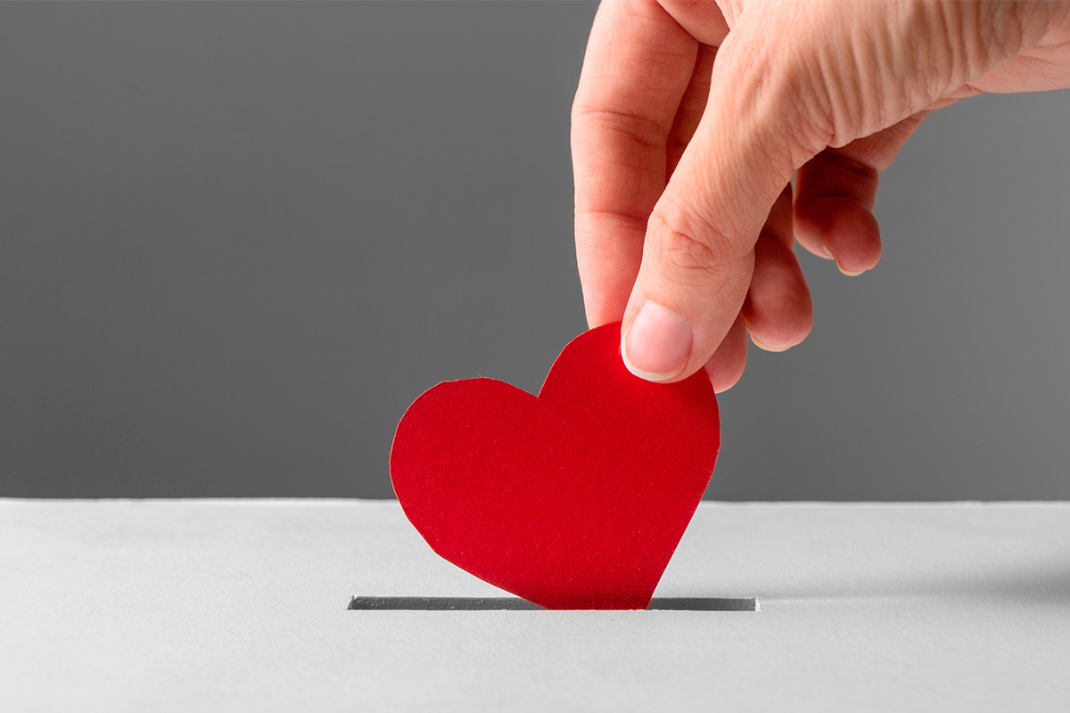 A hand gently puts a red heart into a box, representing love and care for families overcoming trauma.