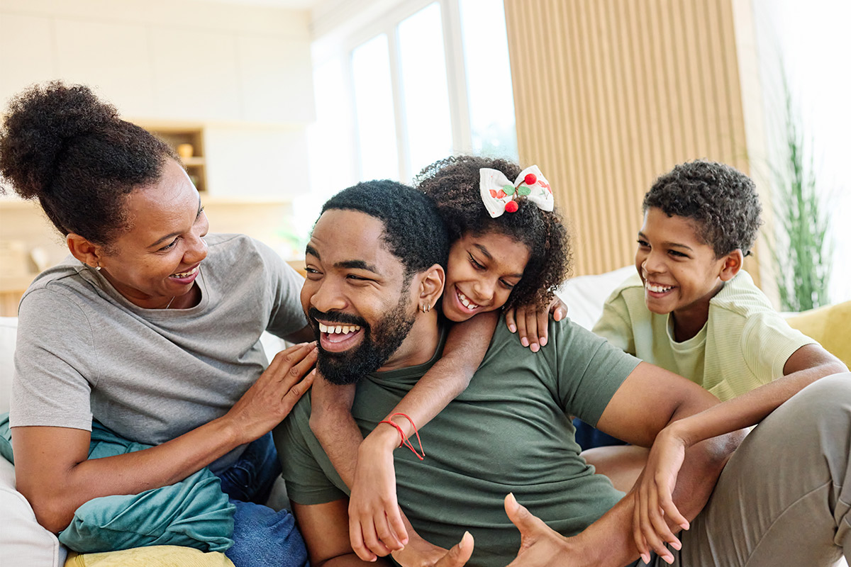 A family of four sitting together on a couch, smiling and enjoying quality time, emphasizing healthy co-parenting boundaries.