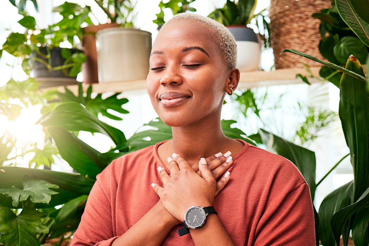 A woman with hands clasped in front of vibrant plants, representing new possibilities for healing and hope in the New Year.