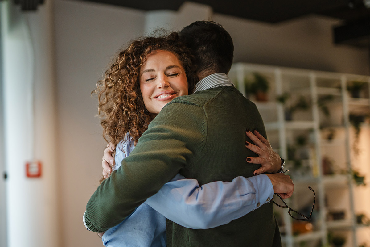 In an office setting, a man and woman share a warm hug, representing love and healing in relationships post-trauma.
